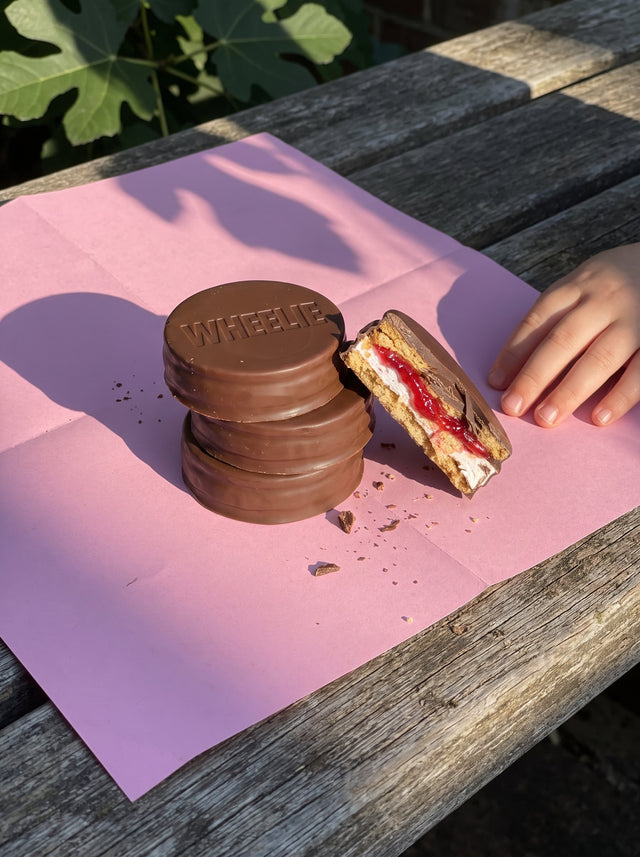 Stacked Wheelies on pink paper in afternoon sun, one broken to show biscuit, marshmallow and raspberry jam