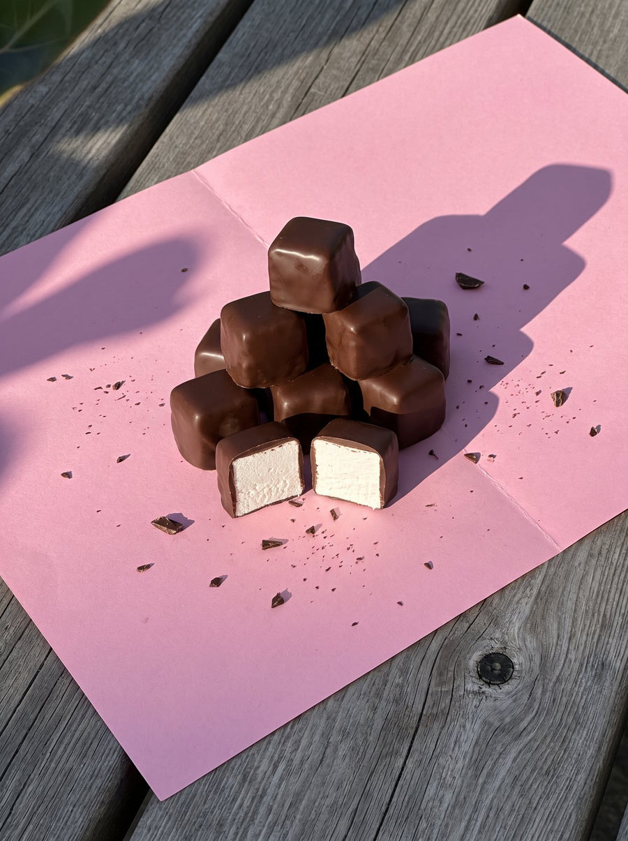 Choc coated marshmallows on pink paper in afternoon sun, one cut in half
