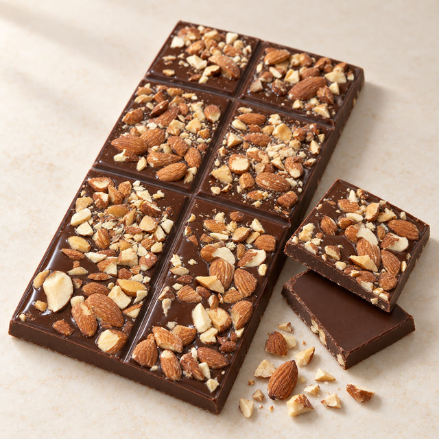 Vegan almond bar: a moulded dark chocolate block covered in roasted chopped almonds, with two squares snapped off showing the plain chocolate underside