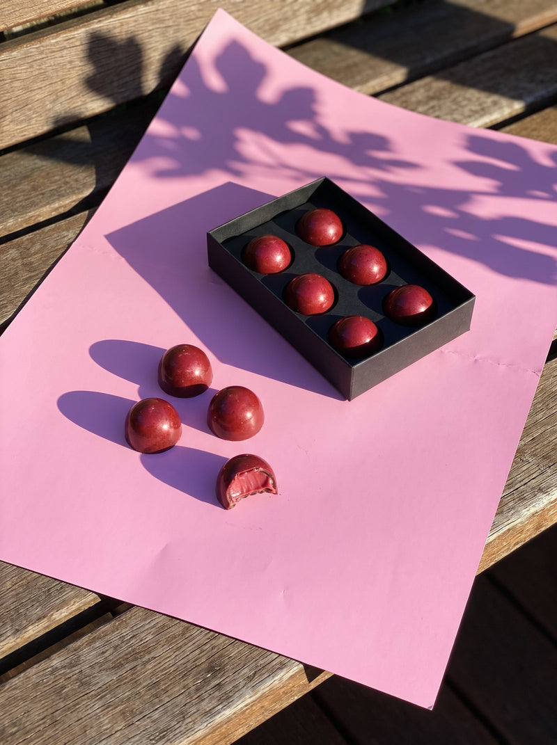 Raspberry bon bons rolling out of their tray onto pink paper