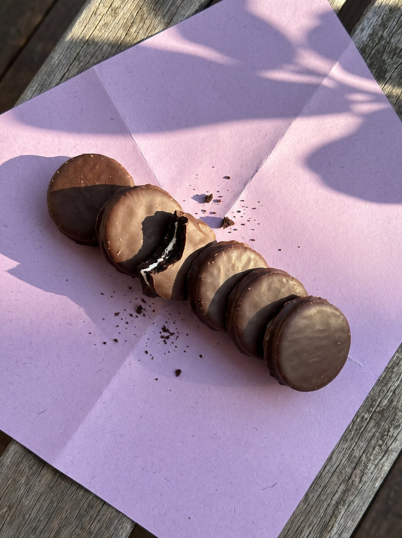 Chocolate coated Oreos on lilac paper, one bitten