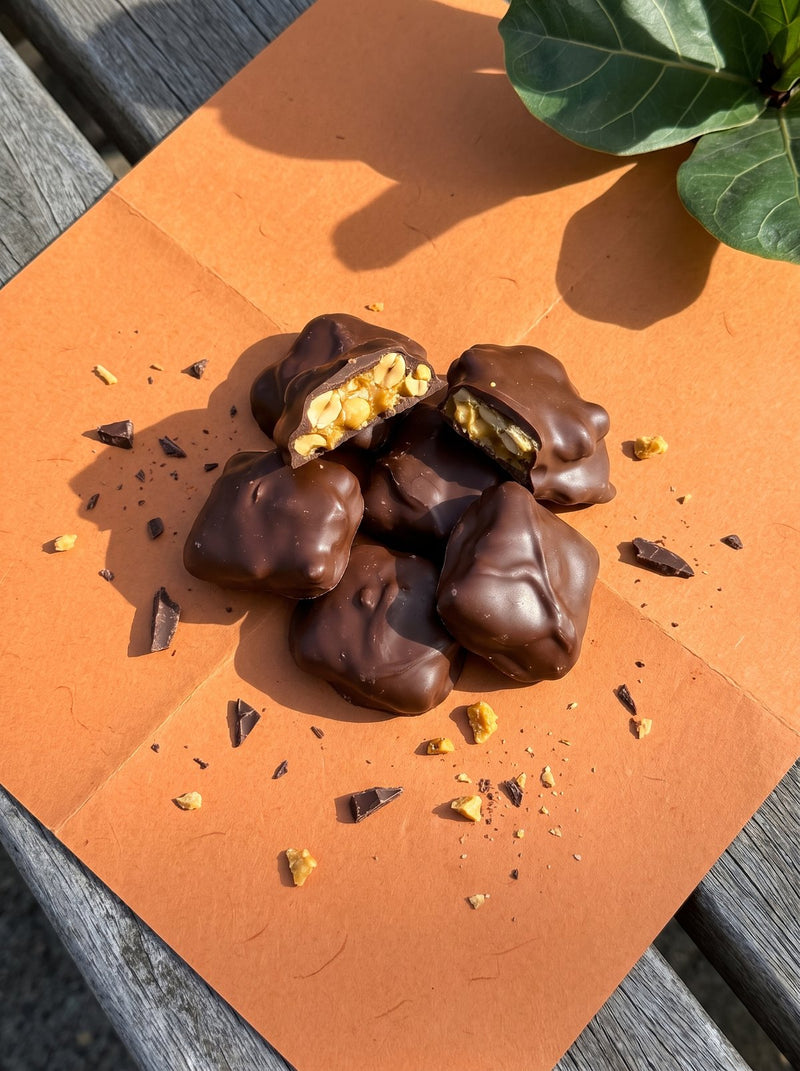 Choc coated peanut brittle on orange paper, one piece snapped open