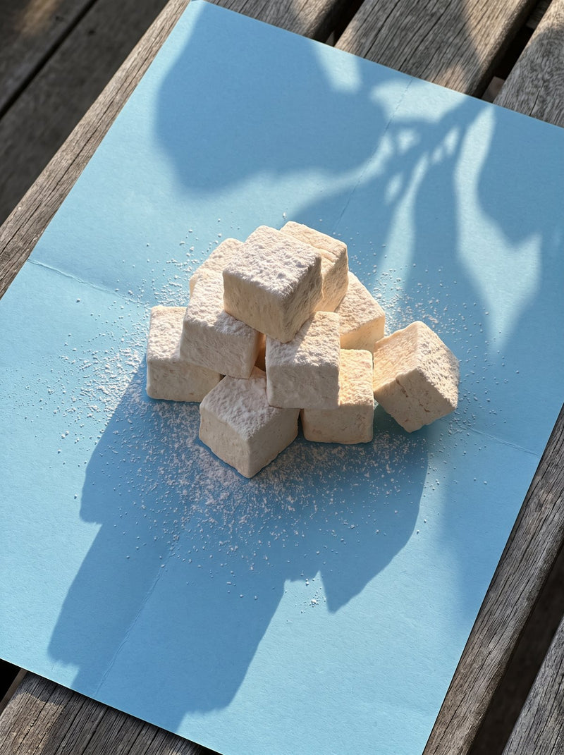 Vanilla marshmallows dusted with icing sugar on blue paper